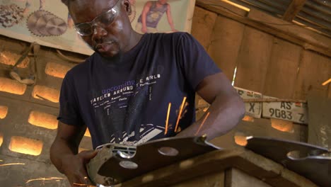 African-American-Male-Works-Welding-a-Metallic-Saw,-Ghana-Wooden-Cabin-Workshop