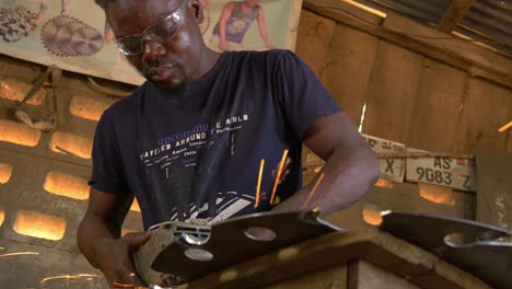 hombre afroamericano trabaja soldando una sierra metálica, taller de cabañas de madera en ghana