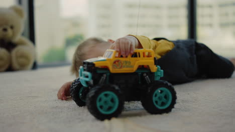 Cheerful-boy-lying-on-rug-with-toy-truck.-Baby-playing-with-toy-car-at-home.