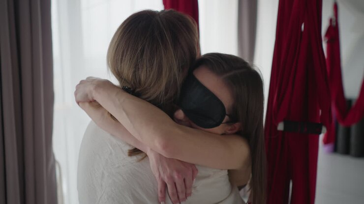 Practitioner hugging partner tightly during mindful wellness session in serene studio space with aerial silks and soft natural light, sharing emotional connection and supportive embrace