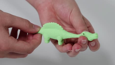 close-up of hands stretching and manipulating a flexible green toy dinosaur.