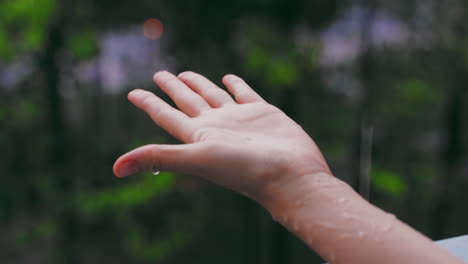 Beautiful-girl's-hand-playing-with-rain-shower-in-the-garden,-blurred-garden-in-the-background