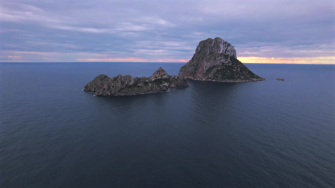 Ripresa aerea in 4K con drone di Es Vedrà al tramonto, Ibiza, Spagna. L'iconica isola rocciosa emerge dal Mar Mediterraneo mentre una calda luce dorata illumina la costa e le acque circostanti