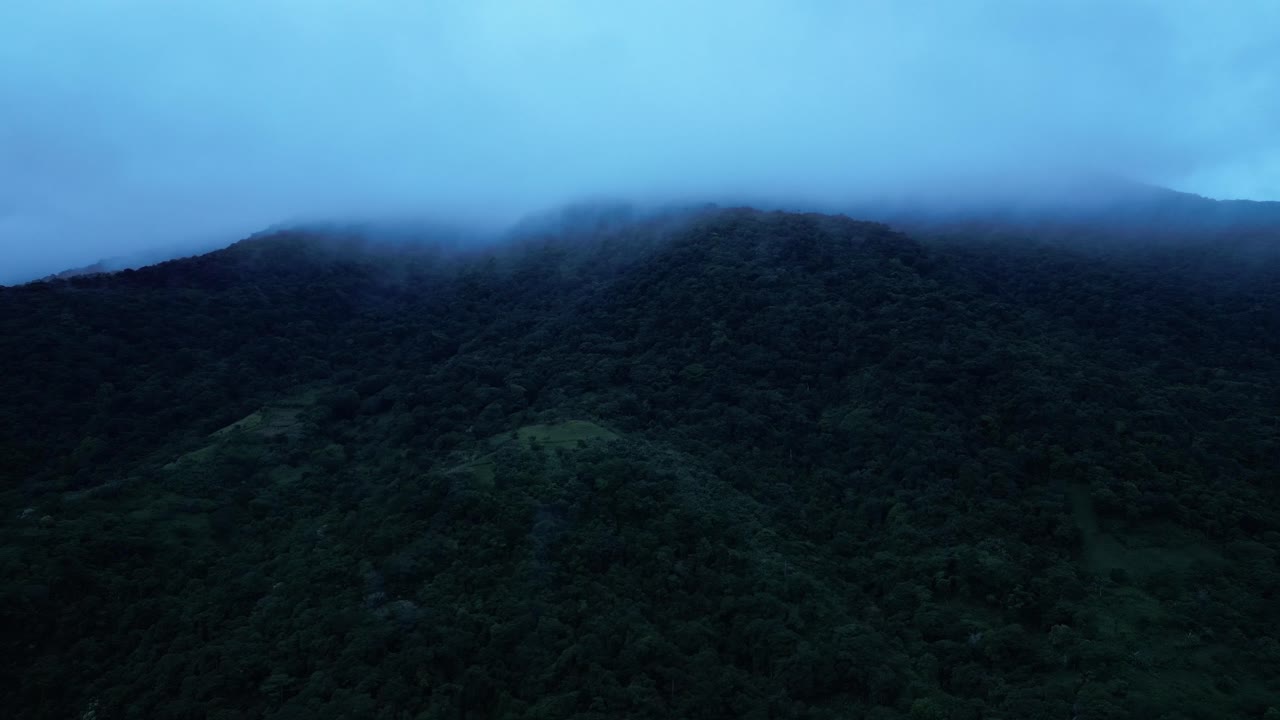 Plano aéreo com drone sobre montanhas tropicais cobertas de névoa, revelando um denso dossel de floresta tropical verde e picos dramáticos envoltos em névoa em uma paisagem melancólica e serena no Monte Banahaw, província de Quezon, Filipinas