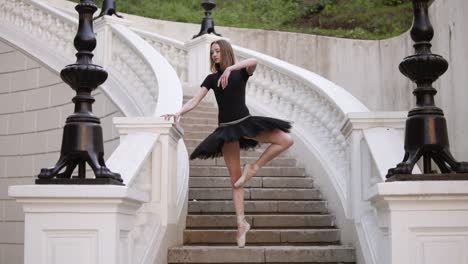 slow motion of a young blonde girl in tutu standing on a beautiful white stairs outside on the street. posing, practicing ballet movements