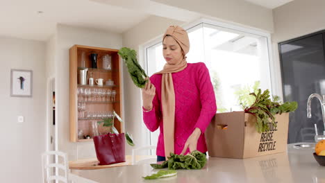 biracial woman in hijab with grocery shopping in kitchen at home with copy space, slow motion