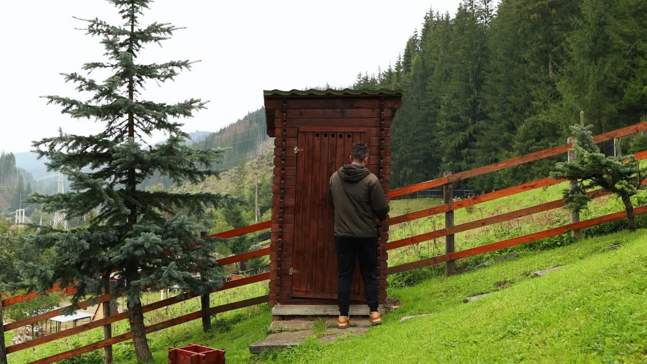 el hombre abre la puerta y entra en un baño rústico de madera al aire libre
