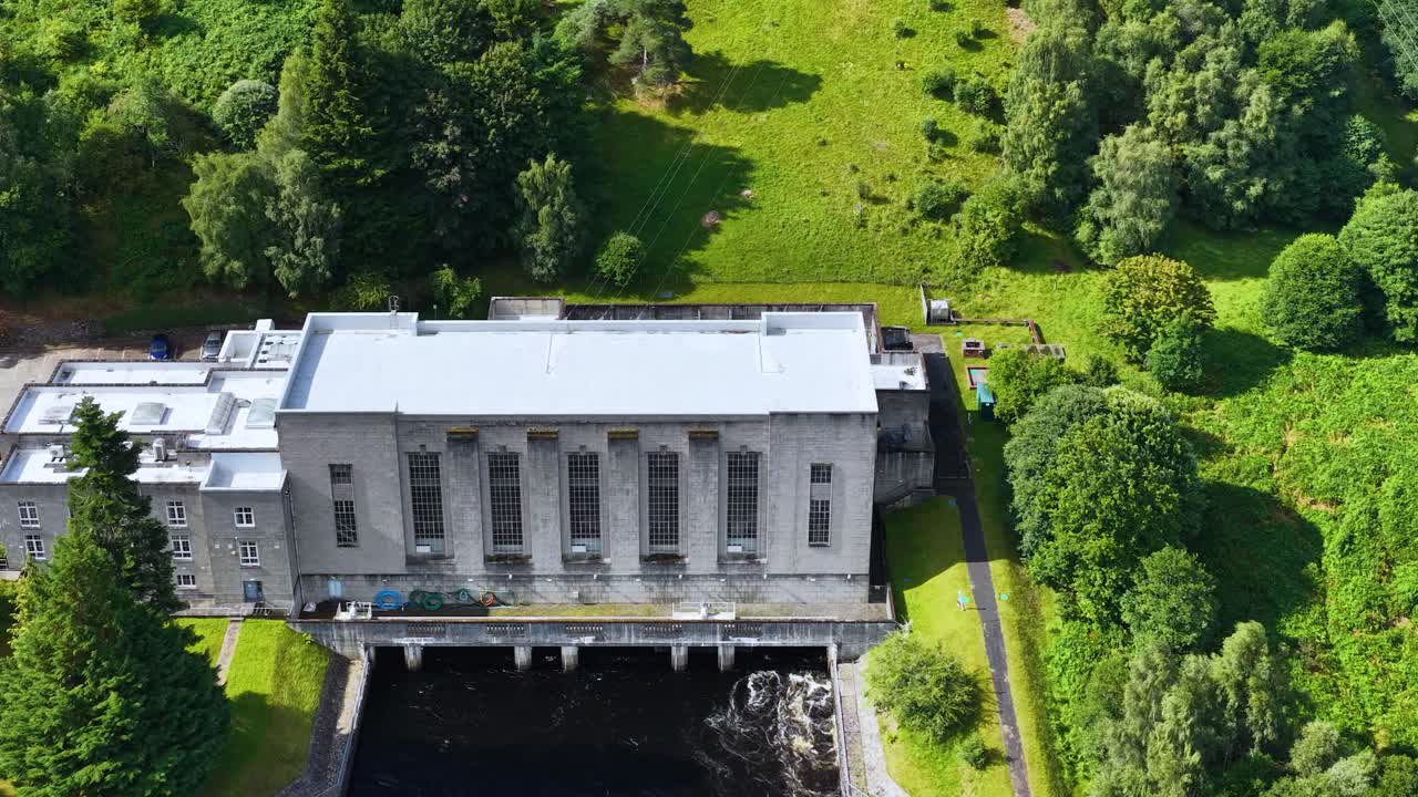 Drone slowly ascends above hydroelectric power station, lush green landscape, bright daylight, stable shot