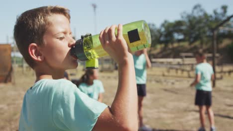 niño caucásico bebiendo agua en el campamento de entrenamiento