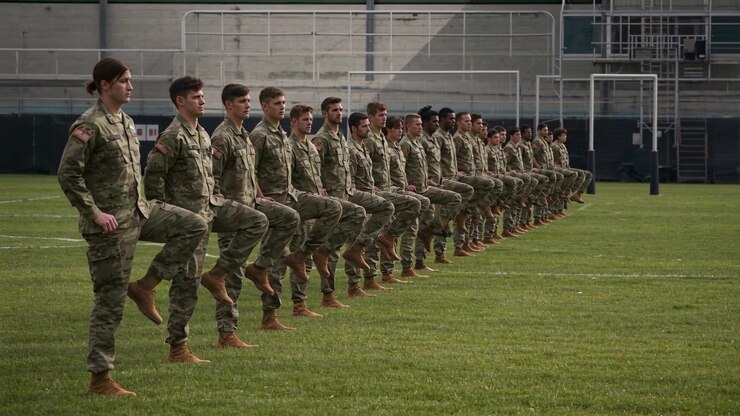 Soldati che eseguono sollevamenti del ginocchio destro a comando su un campo d'erba, con uniformi mimetiche e stivali, durante l'addestramento