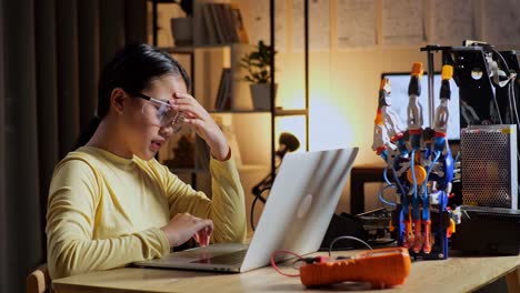 teen asian girl having a headache while working about a cyborg hand on a laptop at home