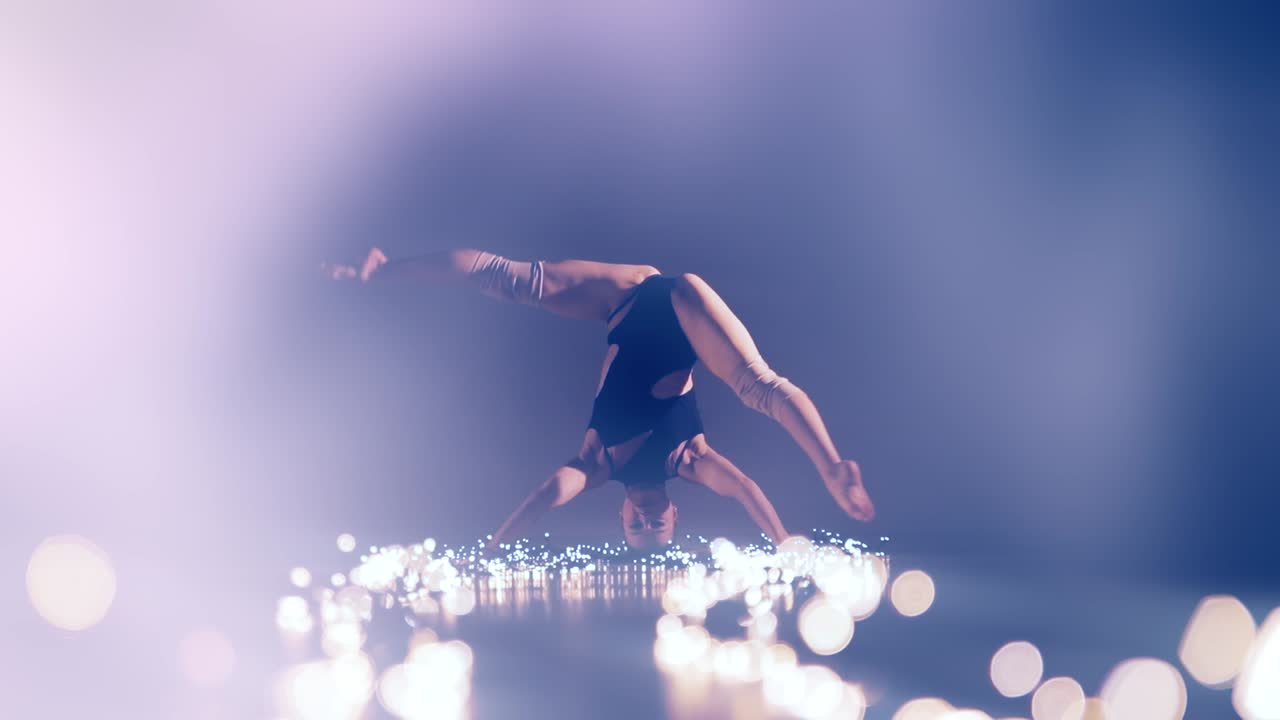 A dancer performs an impressive handstand surrounded by glowing light particles, creating a magical and graceful atmosphere demonstrating power and confidence
