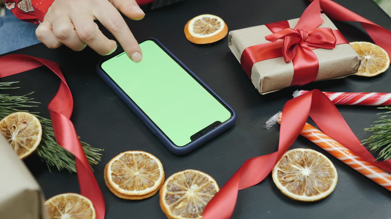 las manos están buscando regalos de navidad en línea en el teléfono inteligente con pantalla verde. compras de vacaciones. descuentos de año nuevo. compras de regalos de navidad en línea. la mujer está comprando regalos en línea con teléfono móvil