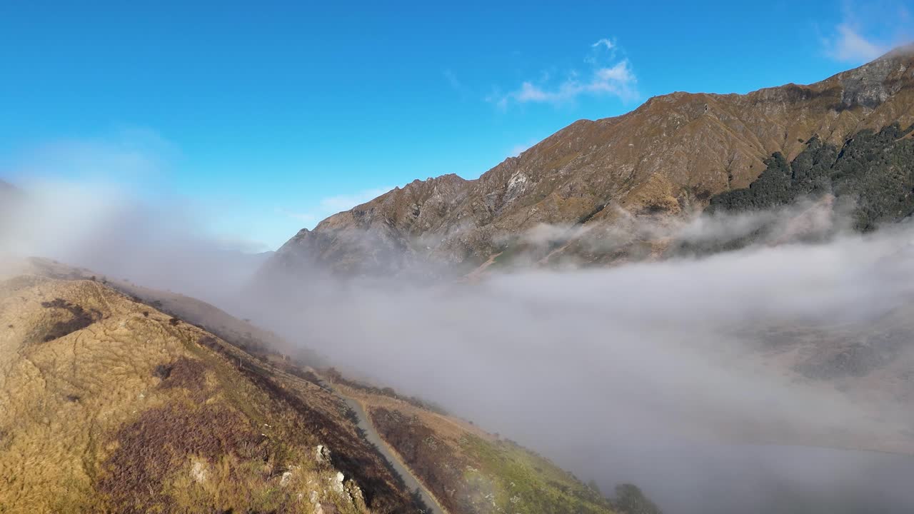Aerial view of Queenstown's mountains enveloped in mist, captured during sunrise with clear blue skies and golden lighting