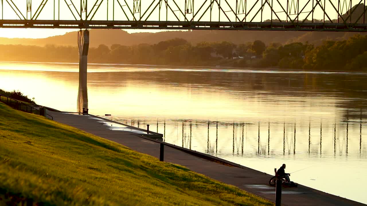 A lone man fishes on a riverbank during golden hour. Beautiful natural light
