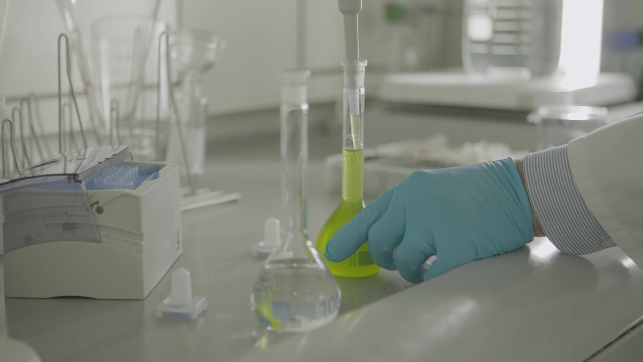 Mano guantata che dosa liquido con pipetta in vetreria da laboratorio su bancone