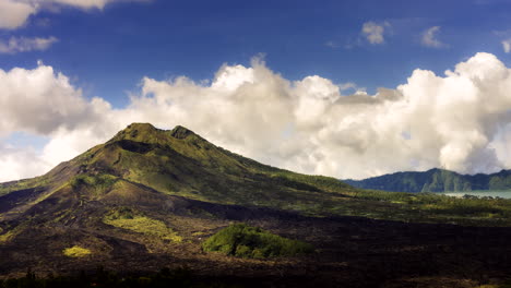 clouds rise up in sky casting dark shadow on grass slopes of mount batur, bali indonesia