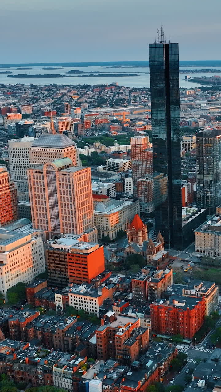 Black shiny skyscraper standing out in the cityscape of Boston. Panorama of the beautiful city at sun down. Rivers at backdrop.. Vertical video