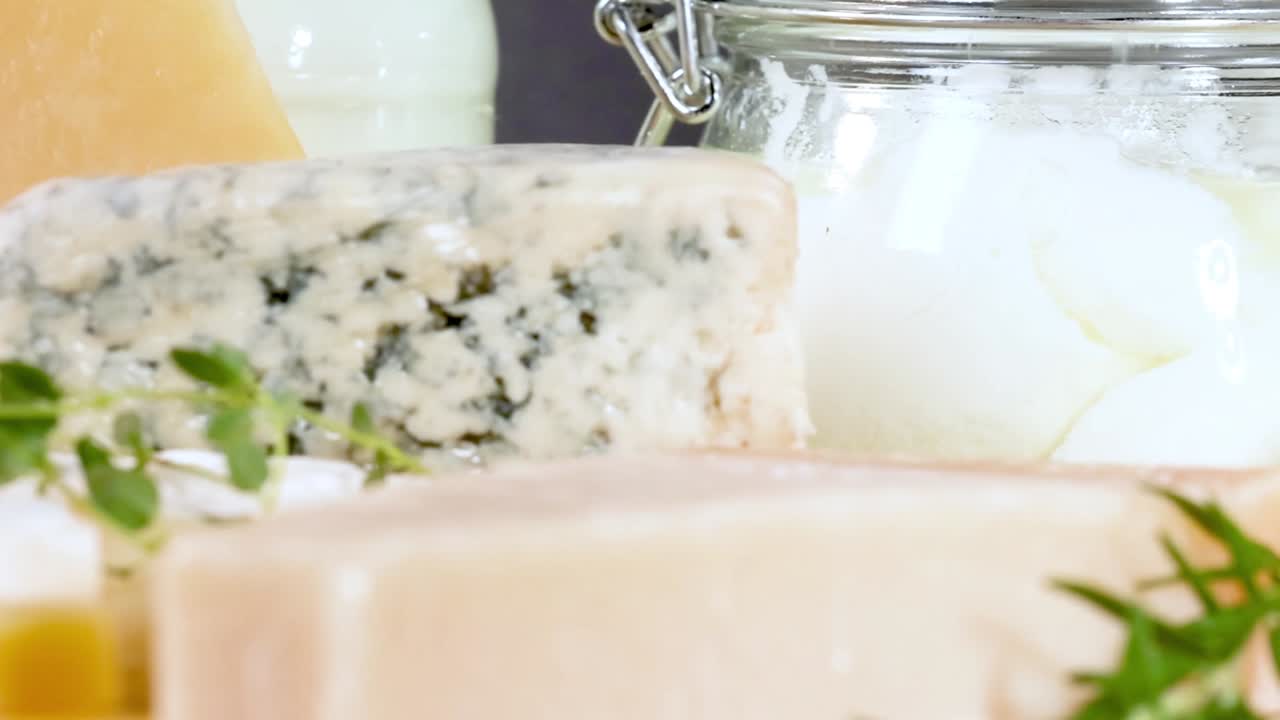 A variety of cheeses and sealed dairy jars arranged with fresh herbs on a black background.