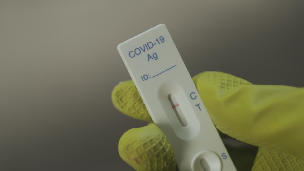 A hand in a rubber glove shows a negative test for a covid