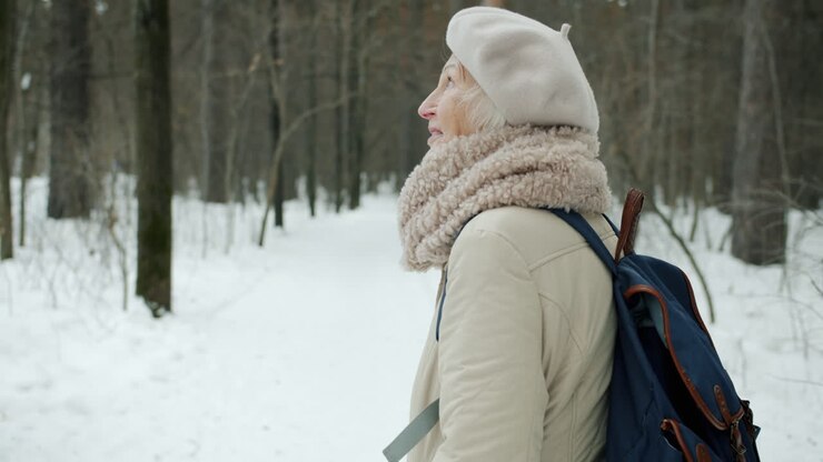 Donna anziana che fa escursioni in una foresta innevata.