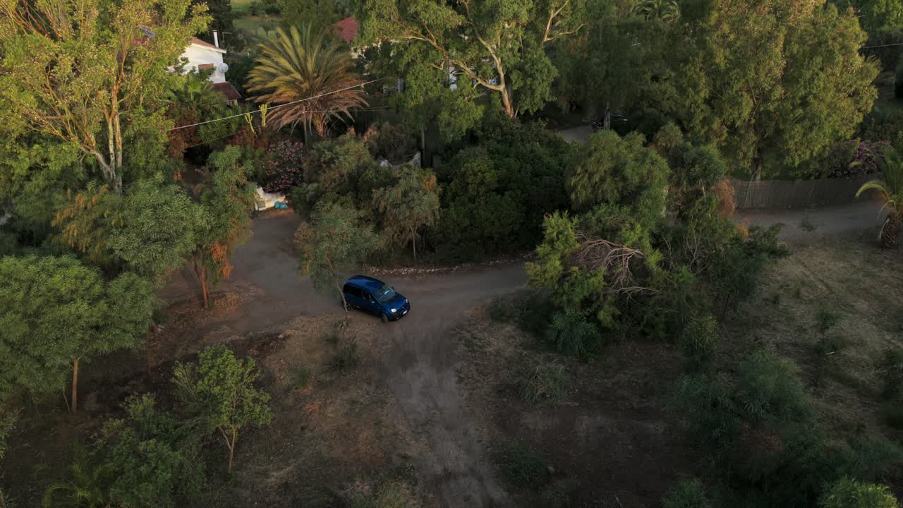 Ripresa aerea con drone dall'alto di un'auto scura parcheggiata su un sentiero sterrato circondato da alberi verdi e rigogliosi e vegetazione mediterranea. Scena rurale tranquilla a Pula, Cagliari, Sardegna, Italia.