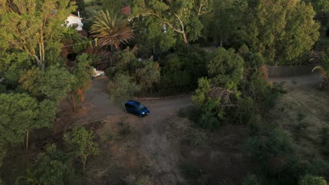 high angle aerial drone shot of a dark car parked on a dirt path surrounded by lush green trees and mediterranean vegetation. peaceful rural scene in pula, cagliari, sardinia, italy