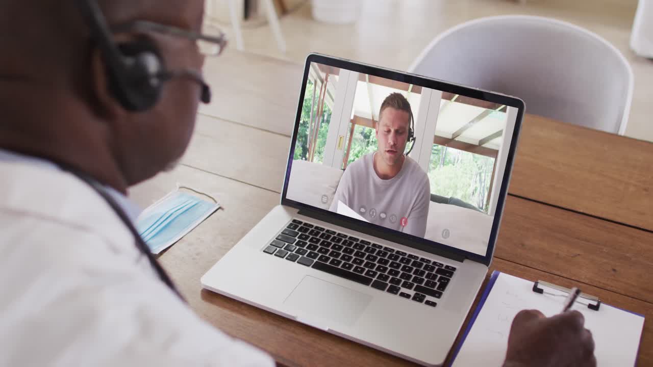hombre de negocios afroamericano sentado en un escritorio usando una computadora portátil haciendo una videollamada con un colega masculino