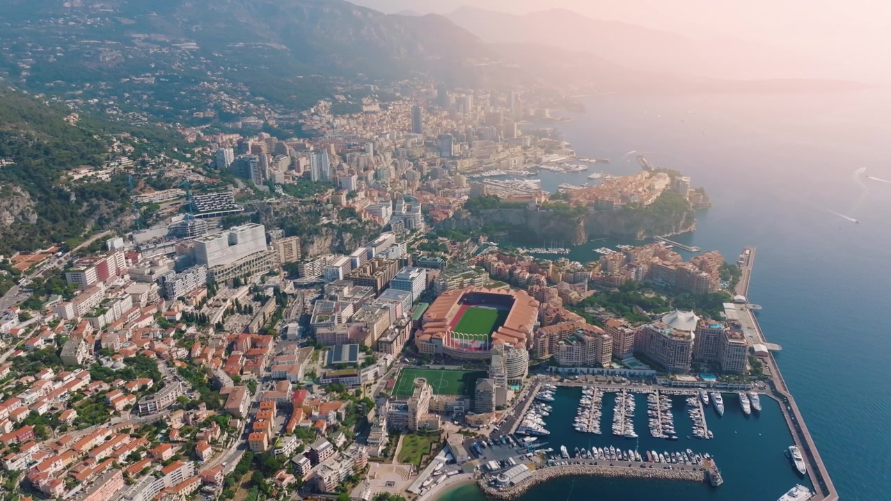 Monaco presenta una costa mozzafiato con yacht nel porto. Il video mette in evidenza le strutture cittadine e le colline circostanti nel tardo pomeriggio. Sono visibili vari edifici e parchi