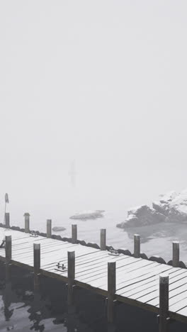 Snow covered dock near a red cabin in a foggy winter landscape