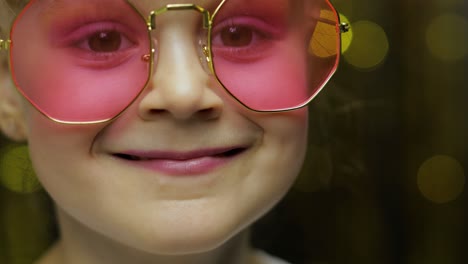 Close-up-face-of-child.-Smiling,-looking-at-camera.-Girl-in-pink-sunglasses-posing