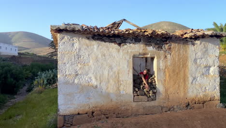 From-an-old-stone-house-near-Betancuria,-woman-gazes-out-of-the-window