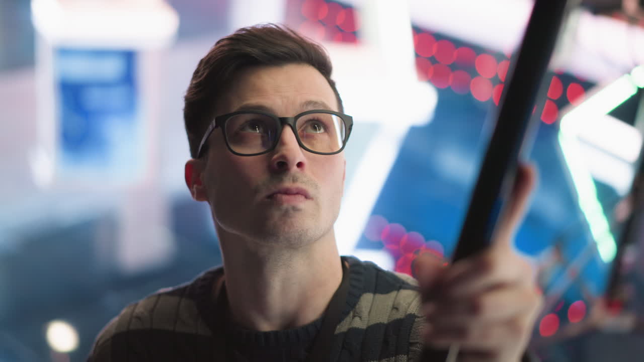 Close-up of man adjusting boom microphone in studio, focusing on sound recording equipment, with neon lighting in background, preparing for professional video production process