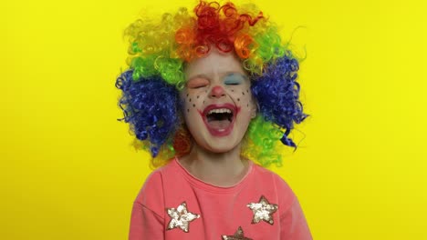 little child girl clown in colorful wig making silly faces. having fun, smiling, laughing. halloween