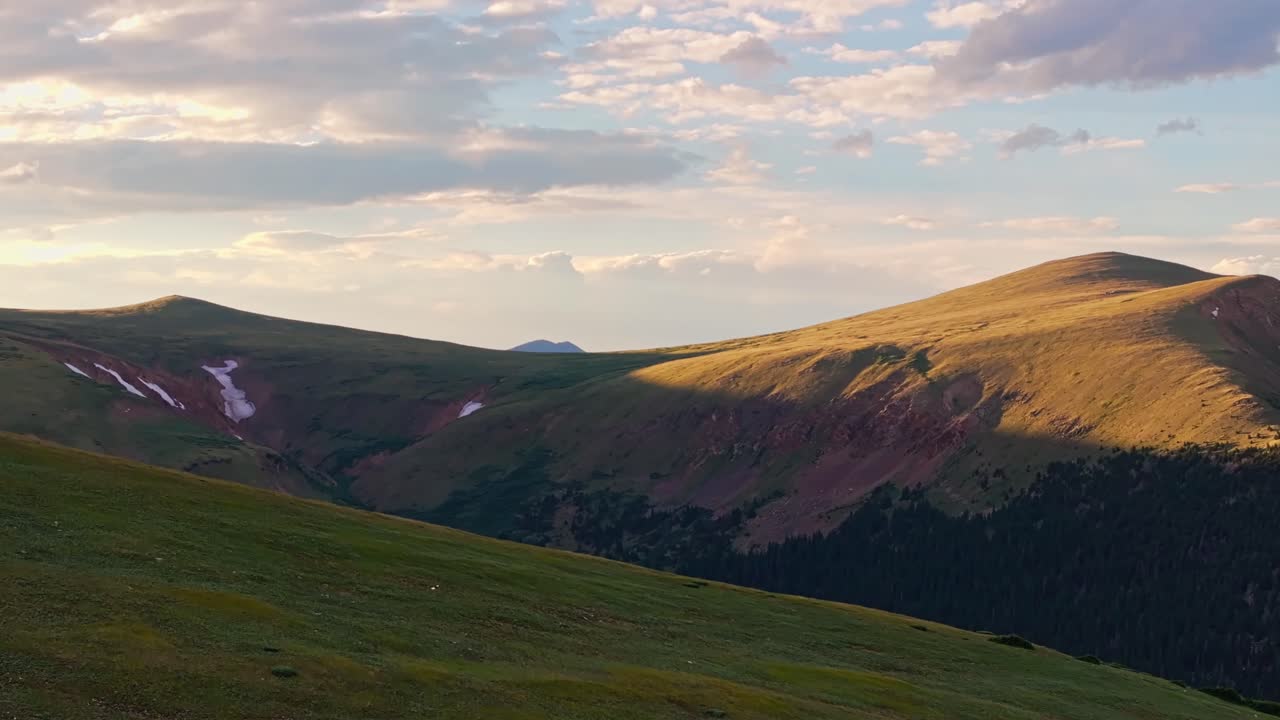 el ascenso aéreo revela por encima de las montañas cubiertas de hierba a los amplios picos de colorado en la hora dorada del atardecer