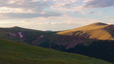 aerial rising reveal above grassy mountain to sweeping colorado peaks at golden hour sunset