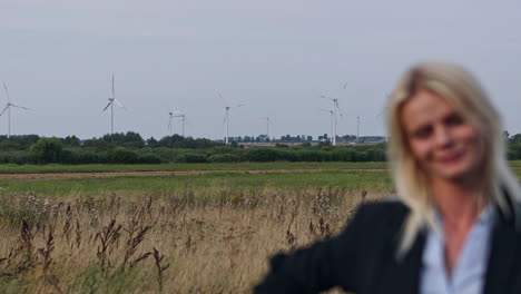 pan shot of pretty business woman smiling into camera,outdoor on farm field with windmill in background