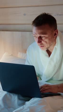 man working late at night on laptop in cozy bedroom with soft lighting