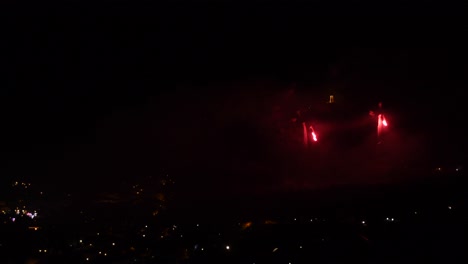 celebración con fuegos artificiales rojos, sobre un pueblo de montaña, por la noche