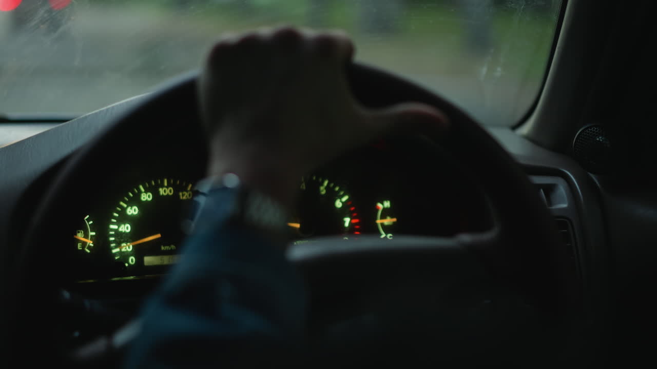 hands on steering wheel, gauges glowing through rainy windshield wristwatch catches green light while driver navigates slick street, tense commute vibe for courier, rideshare driver or late shift