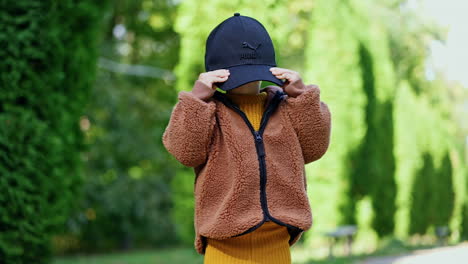 funny little kid playing with a black cap too big for him. cute baby boy in the green park.