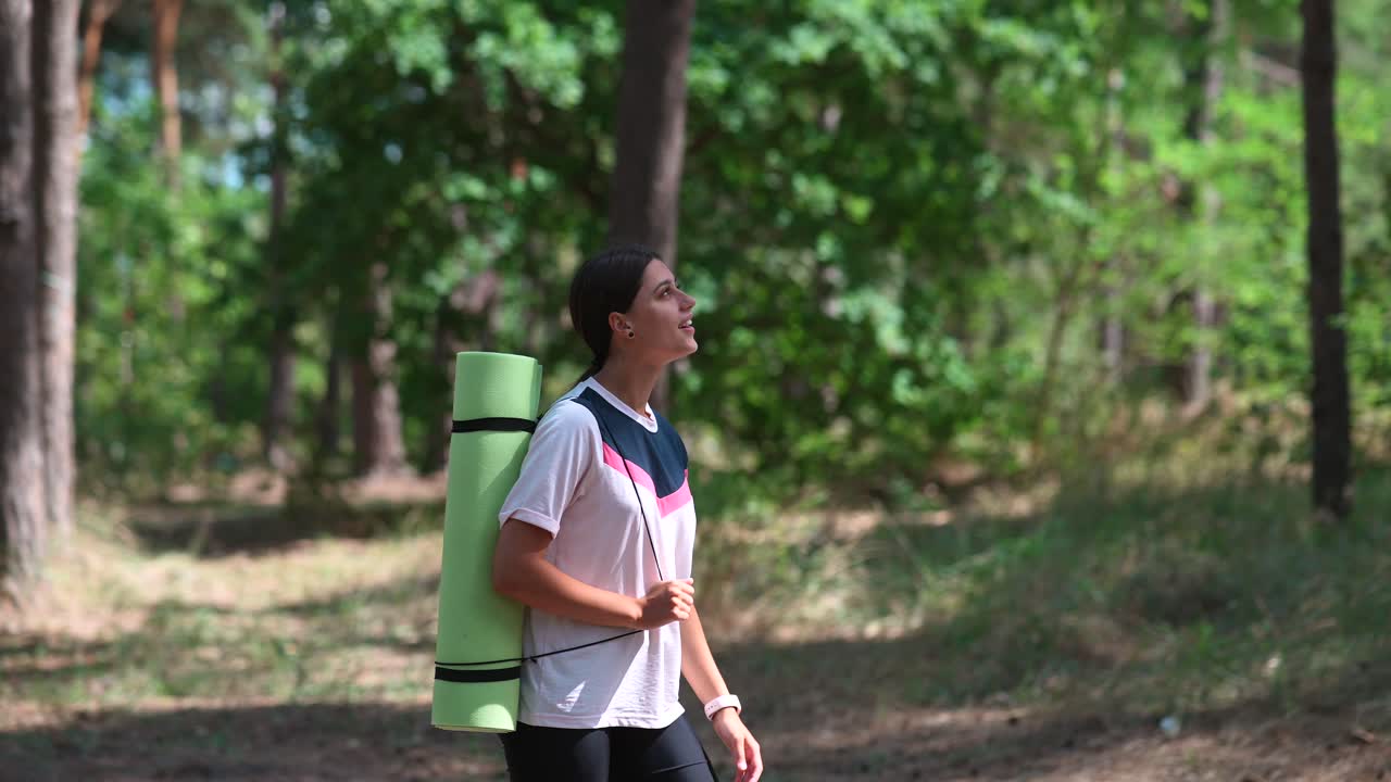 요가 매트 를 가진 여자 가 숲 에서 산책 하고 있다