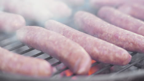 macro de cámara lenta de salchichas a la parrilla en parrilla de barbacoa ardiente y ahumada