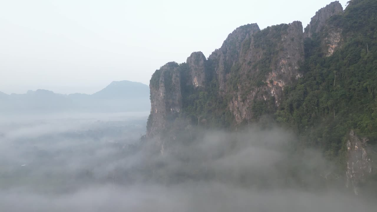 drone disparado volando hacia acantilados envueltos en niebla en vang vieng, la capital de la aventura de laos