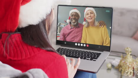 mujer caucásica con sombrero de santa teniendo llamada de video portátil con una pareja diversa