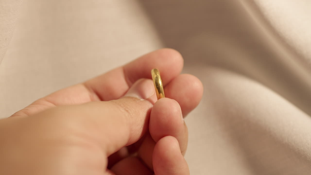 Close-up of an individual holding a gold wedding band, carefully inspecting it for flaws or imperfections
