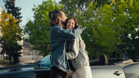 A-happy-couple-of-a-guy-and-a-brunette-girl-in-denim-jackets-stand,-hug-and-look-at-the-camera-against-the-background-of-a-gray