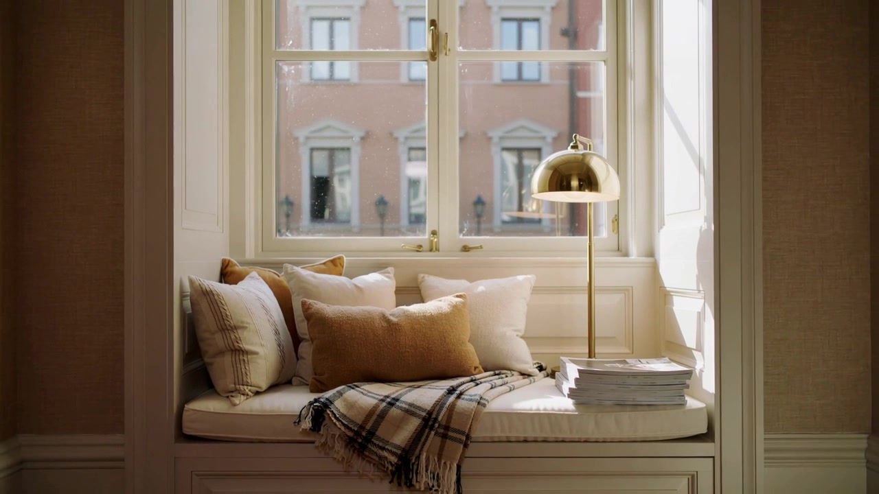 Streaming sunlight bathing window seat at home showing pillows, throw, magazines, brass lamp