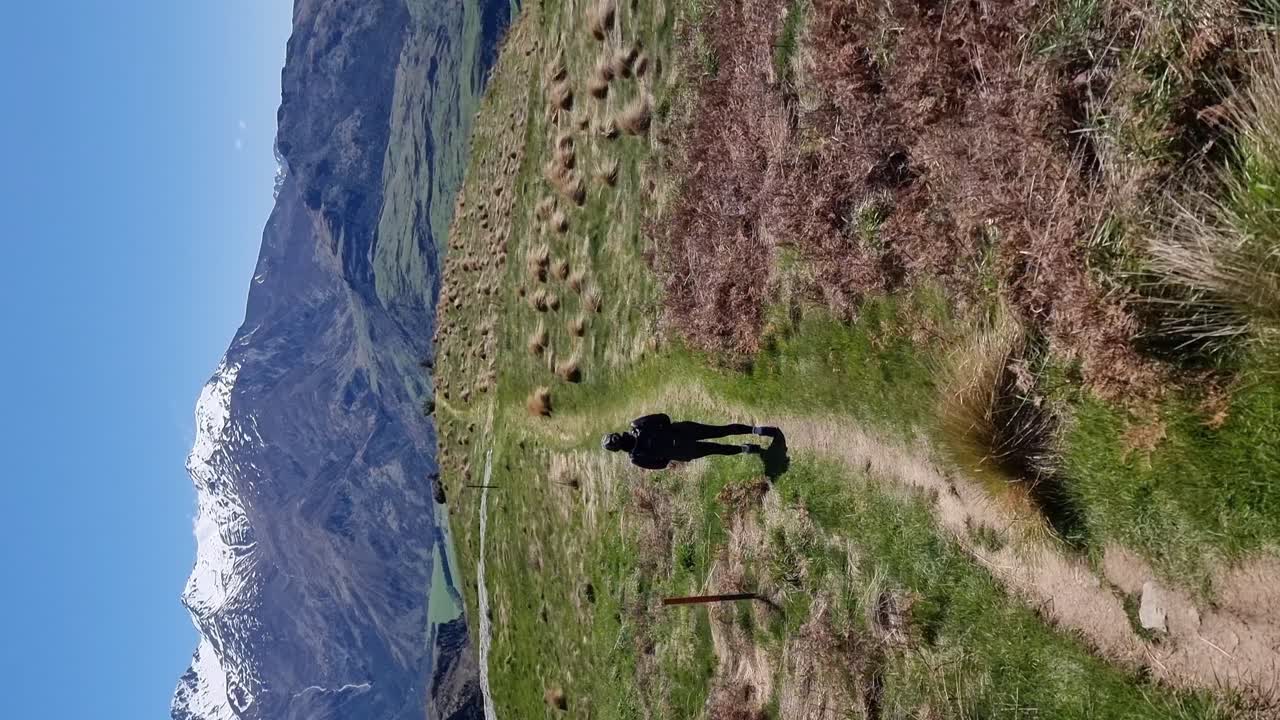 Vertical of a woman walking in a hke with tussock grassland and snow capped mountains in Wanaka New Zealand