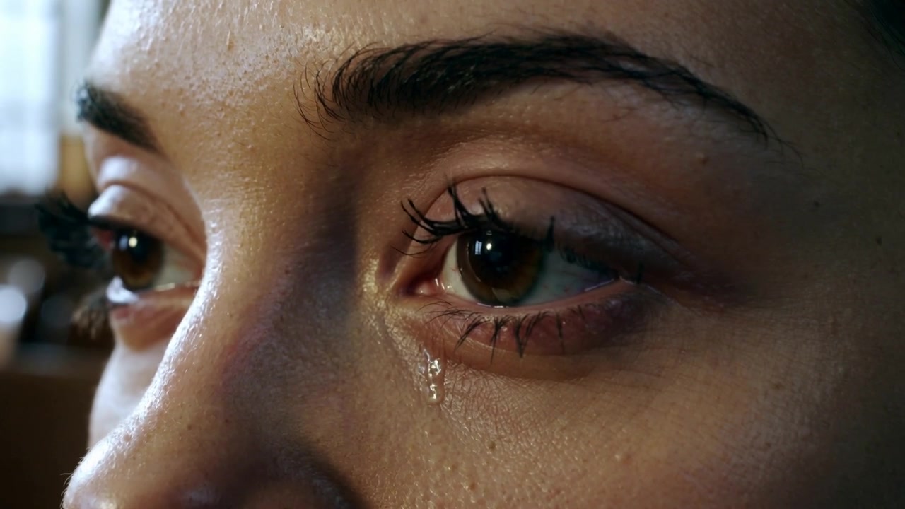 Blinking adult female shedding tear from window light in chapel, mascara lashes reflecting